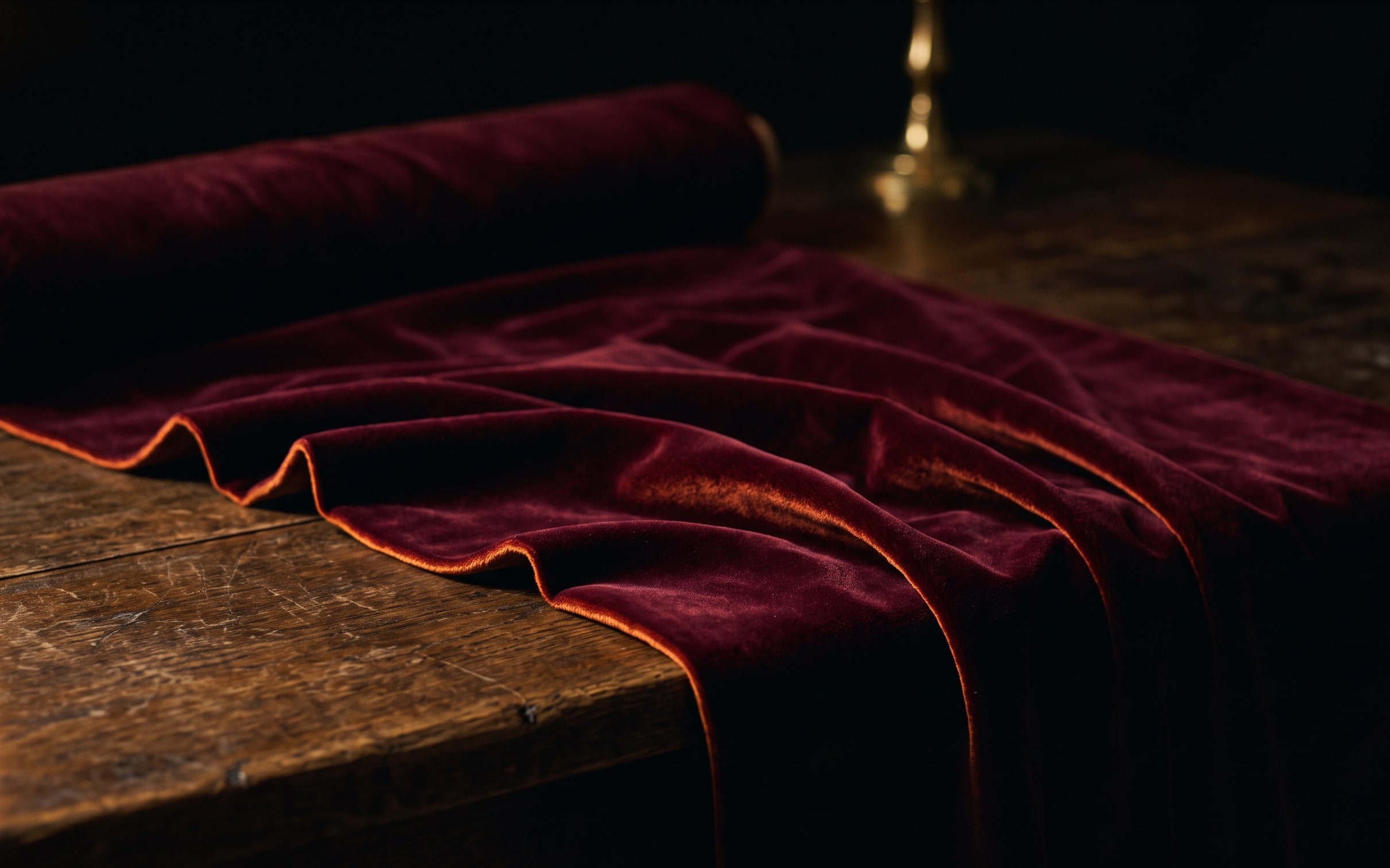 Deep bordeaux velvet in raking candlelight, the pile catching along one fold